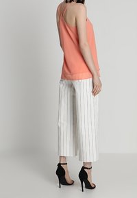 Top sans manches pêche avec de fines bretelles, associé à un pantalon large blanc à rayures et des sandales à talons noirs.