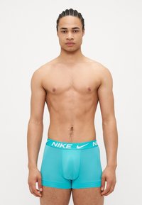 Boxeri Nike turcoaz, cu un elastic alb cu marcaj, având o croială strânsă și o textură netedă.