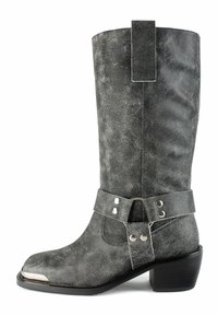 Botas western de cuero negro desgastado hasta la mitad de la pantorrilla con puntera de metal, correa de arnés con tachuelas plateadas y tacón apilado.