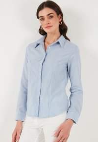 Camicia button-up a righe blu e bianche con colletto a punta e maniche lunghe. Presenta una vestibilità slim, una texture liscia e una leggera lucentezza.