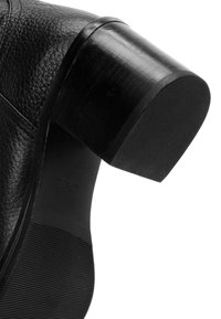 Bottine en cuir noir avec un dessus texturé, un talon cylindrique, une semelle en caoutchouc avec des nervures et un accent noir lisse autour du talon.