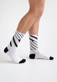 Schwarz-weiße gestreifte Knöchelsocken aus einem atmungsaktiven Stoff, mit einer einfarbigen schwarzen Zehen- und Ferseneinlage.