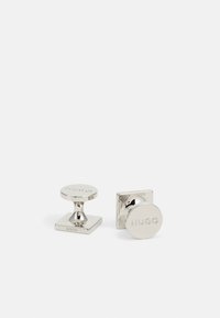 Silver-tone cufflinks with a circular and square design. One features an engraved logo, smooth texture, and polished finish.