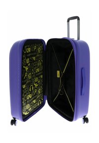 Valise rigide violette avec un extérieur texturé, double roulettes et un intérieur doublé d'un motif vert vif comportant des icônes. Compartiment interne noir visible.