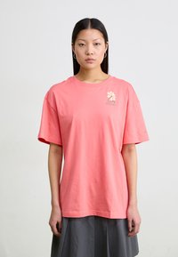 Koraalroze t-shirt met korte mouwen en een ontspannen fit. Kenmerkt zich door een bloemenlogo in lichtbeige op de borst. Zacht katoenen materiaal.