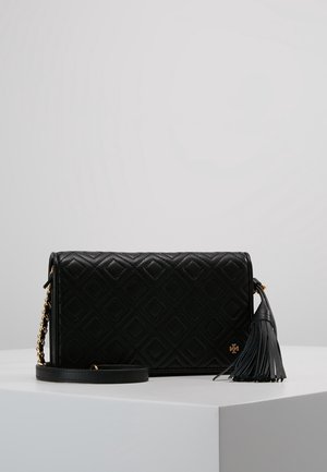 Sac bandoulière en cuir noir matelassé avec bandoulière chaîne dorée et détail de pompon en cuir sur un socle blanc.