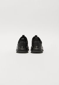 Baskets de sport noires avec une texture lisse, un bout arrondi, un col de cheville rembourré et une semelle texturée. Comprend des tirettes sur les talons.
