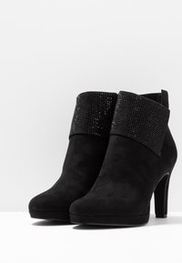 Mustat nilkkurit, joissa on mokkanahkainen viimeistely ja kimalteella koristeltu varsi. Sisältää hieman teräväkärkisen varren ja korkean korot.