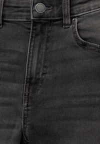 Jeans de mezclilla negra con un diseño clásico de cinco bolsillos, textura sutil y un cierre frontal con botón de metal y detalles de costura en contraste.