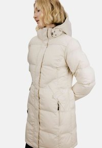 Pufferjakke i lys beige med høy krage og glidelås foran. Teksturert, quiltet design med sidelommer og justerbar hette.