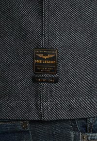 Camicia di denim con un motivo a righe bianche e nere. Presenta un'etichetta gialla e nera con la scritta "PME LEGEND" accompagnata da ali e dettagli del prodotto.