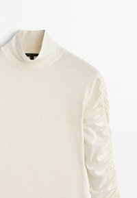 Cremefarbener Langarmtop mit hohem Kragen, der über Raffung an den Ärmeln verfügt, aus weichem, leichtem Stoff gefertigt.