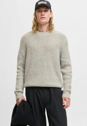 Lichtgrijze gebreide trui met textuur en ribbelpatroon, ronde halslijn en lange mouwen, gecombineerd met zwarte pinstripe broek en vastgehouden met een zwart kledingstuk.