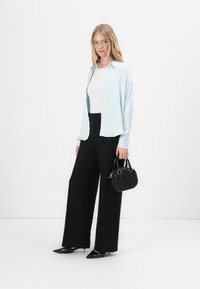 Lichtblauwe button-up cardigan, witte top, zwarte wijde pantalon, zwarte handtas en puntige zwarte schoenen. Gladde stof en taaie pasvorm.
