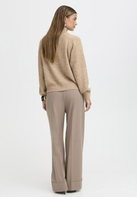 Maglione di lana beige con colletto alto e spalle scese abbinato a pantaloni a gamba larga marrone chiaro con orlo arricciato.