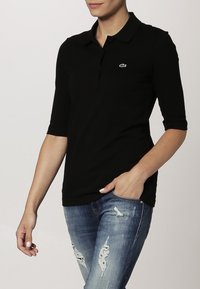 Černé polo tričko s tříknoflíkovou léga a krátkými rukávy. Tkanina je hladká s jemným leskem. Obsahuje malé vyšívané logo.