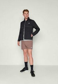 Černá sportovní bunda na zip, šedé tričko, hnědé šortky, černé tenisky a ponožky, s logem a jednoduchým designem.