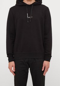 Sweat à capuche noir avec une coupe décontractée. Confectionné en tissu doux, il présente un logo à l'avant, une poche kangourou, ainsi que des poignets et un ourlet côtelés.