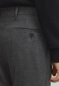 Pantaloni in misto lana grigi con una superficie liscia, dotati di una tasca posteriore con bottone nero e una silhouette slim.