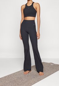 Top corto atletico nero e leggings svasati realizzati in tessuto elastico con una leggera texture. Caratterizzato dal logo Nike in blu scuro.