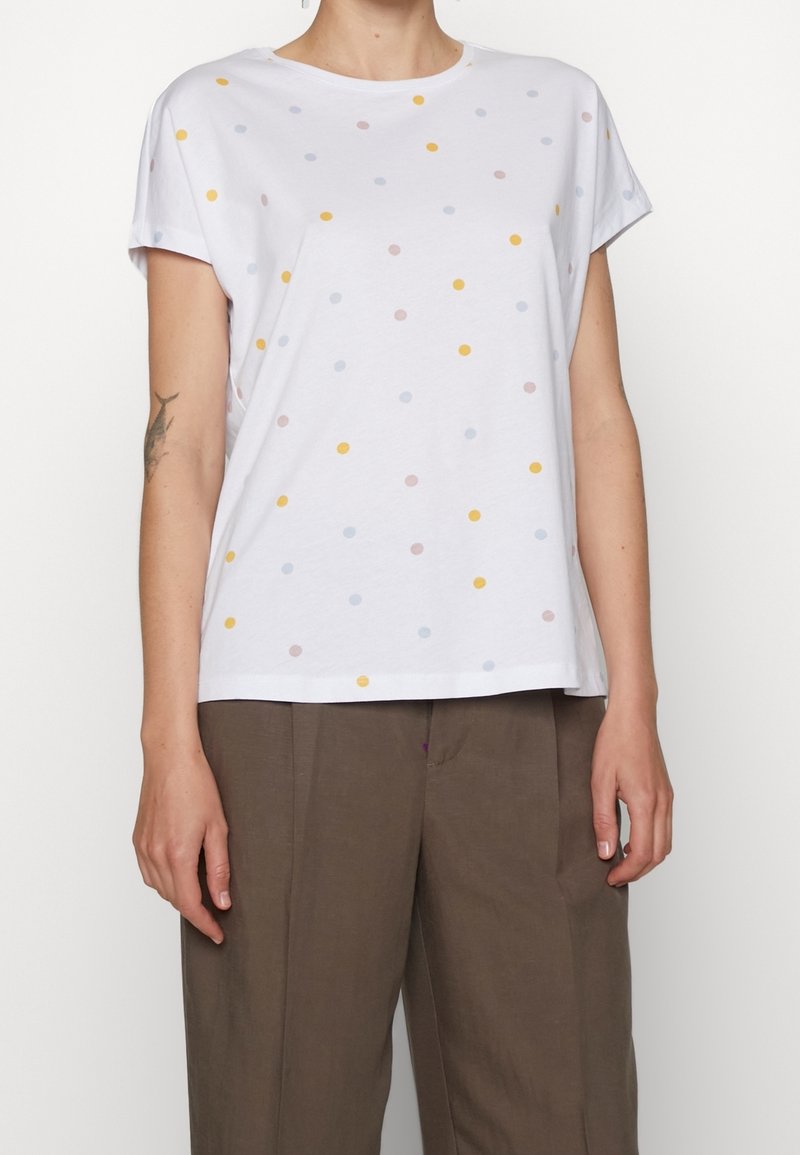 Vit bomull t-shirt med korta ärmar och rund halsringning, med flerfärgade prickar i gult, blått och rosa. Rak fåll.