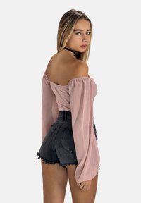 Off-shoulder, lyserød bluse med flagrende ærmer parret med højtaljede sorte denimshorts med rå kanter og lommer.