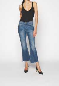 Bodysuit negro de canalé, pantalones de mezclilla claros de campana con dobladillos deshilachados, combinados con tacones negros de punta con herrajes dorados.