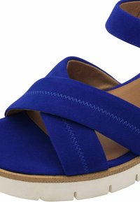 Blue suede sandal with crisscross straps, textured finish, and a contrasting white platform sole. Features detailed stitching accents.