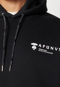 Sweat à capuche noir en mélange de coton doux. Présente un logo blanc et du texte sur la poitrine. Les cordons ont des embouts en métal argenté avec le branding.