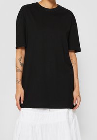 Černé bavlněné tričko s krátkými rukávy, volný střih, kulatý výstřih a hladká textura; nošeno přes bílou, vrstvenou sukni.