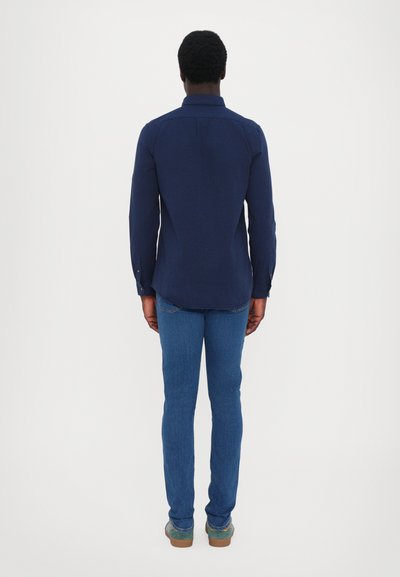 Cămașă bleumarin cu mânecă lungă și manșete cu nasturi, asortată cu blugi de culoare bleu închis și pantofi maro. Material neted, slim fit și design minimalist.