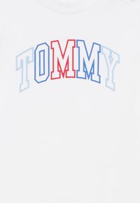 Λευκή φούτερ με την επιγραφή "TOMMY" σε ημικυκλικό σχήμα· τα γράμματα είναι κόκκινα, μπλε και γαλάζια με ελαφρύ διαβαθμισμένο χρώμα. Μαλακό βαμβακερό υλικό.