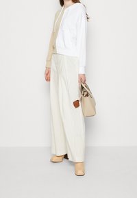 Felpa con cappuccio bianca e beige, pantaloni a righe larghe, tacchi color crema e una borsa beige con accenti marroni.