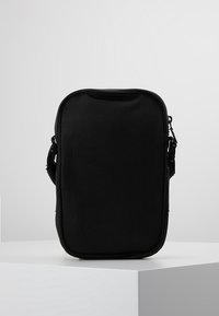 Borsa rettangolare nera realizzata in tessuto resistente. Presenta una chiusura con zip e una tracolla regolabile. Texture liscia senza motivi o dettagli visibili.