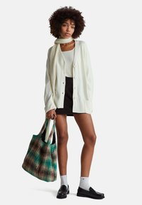 Bílý pletený kardigan s žebrovanou texturou, zapínání na knoflíky, doplněný černou sukní, zeleno-hnědou vzorovanou taškou a černými botami.