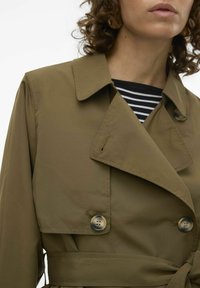 Olivgrön trenchcoat med dubbelknäppning, stor krage och två knappar. Har en knytning i midjan och ett mjukt, lätt tyg.