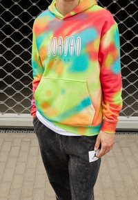 Person wearing a multicolored tie-dye Jordan Nike hoodie and black pants with a white Jordan logo patch standing outdoors on a paved surface.