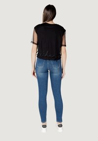 T-shirt nera cropped con maniche in rete e dettaglio testuale "exchange" all'orlo, abbinata a jeans in denim blu aderenti e scarpe bianche.