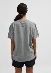 Grå t-shirt med kort ärm och avslappnad passform; har texten "F.U.T." tryckt på ryggen. Materialet verkar mjukt och har en slät textur.