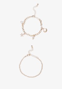 Gouden kettingarmbanden met bedels: een zeester, schelp en kegel, met een parelaccent op de bovenste armband; verstelbaar sluitmechanisme.