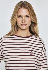Cream and burgundy striped long-sleeve shirt with a round neckline and small embroidered logo on the chest. Soft cotton fabric.