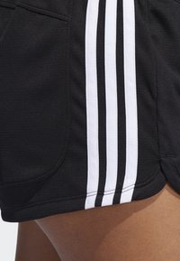Čierne športové šortky so bielymi bočnými pruhmi, vyrobené z ľahkej látky s hladkou textúrou. Obsahujú bočné vrecká a zakrivený lem.