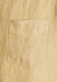 Gros plan d'un tissu en lin beige montrant une poche carrée cousue avec un fond pointu sur un vêtement.