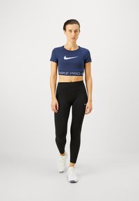 Top corto Nike Pro de color azul marino con logo blanco, combinado con leggings negros de tiro alto y zapatillas deportivas blancas. Diseño simple y ajustado.