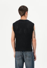 Sort ærmeløs top med ribbet tekstur og lodrette slids. Bagsiden har en rund halsudskæring og en lige skæring, parret med blå jeans.
