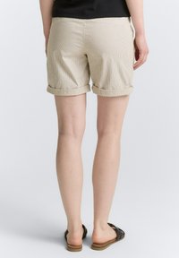 Beige stribede shorts med opkr�øllede manchetter, lavet af blødt stof. Simpelt design uden synlig hardware eller dekorationer. Båret med brune sandaler.