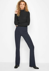 Czarny prążkowany golf połączony z granatowymi spodniami w dzwony. Stylizacja charakteryzuje się dopasowanym krojem, gładką teksturą i minimalnymi detalami.