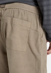 Beige shorts with an elastic waistband, featuring a back pocket and subtle texture. Paired with a gray striped long-sleeve shirt.