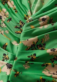 Tissu vert avec un motif floral noir, jaune et blanc, froncé avec des plis cousus visibles et des détails de couture.