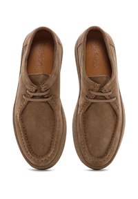 Zapatos de ante marrón con punta redondeada, detalles de cordones y costuras en contraste. Forro interior suave y suela plana. Diseño cómodo.